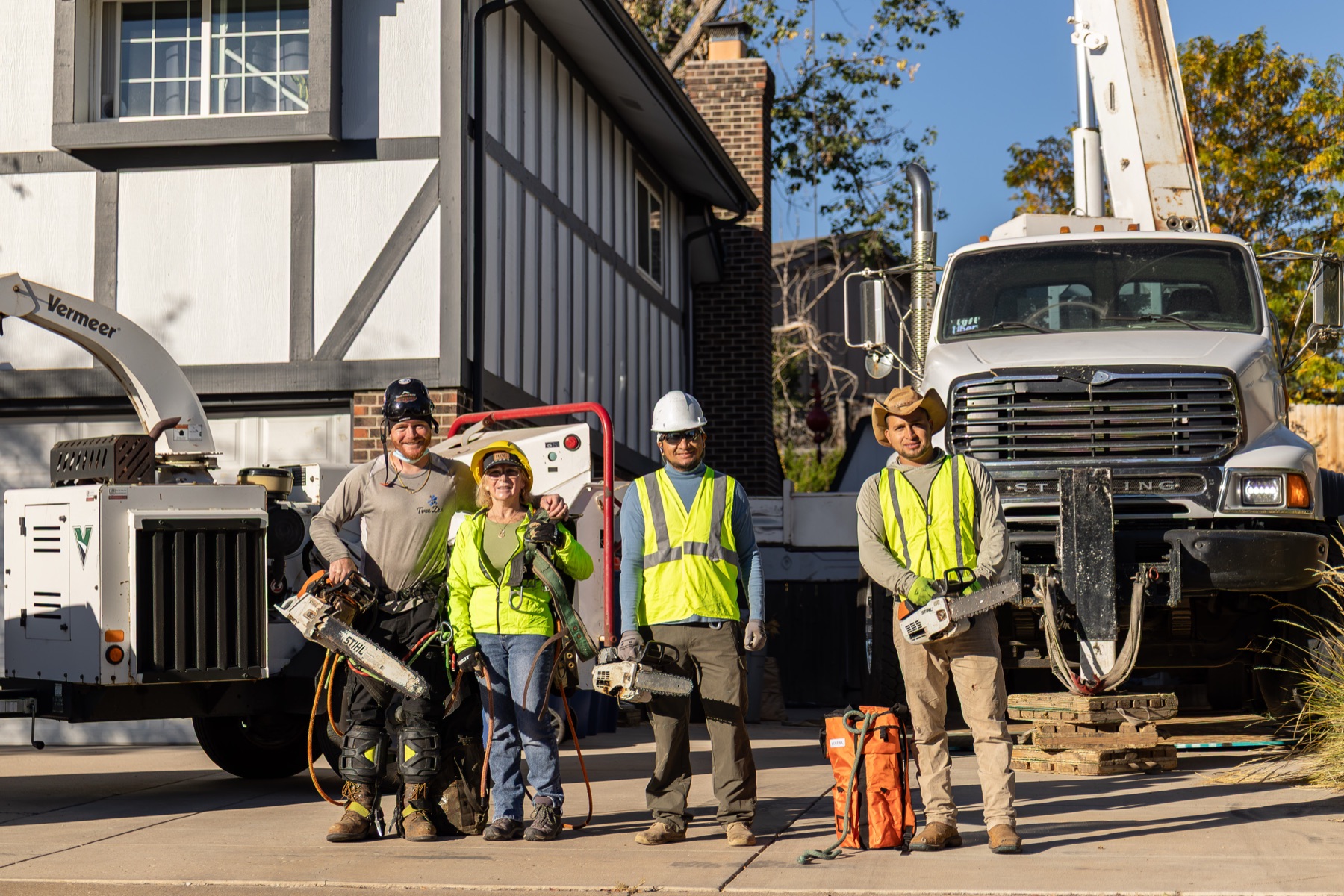 The Tree Zen crew with chainsaws in front of their wood chipper and bucket truck